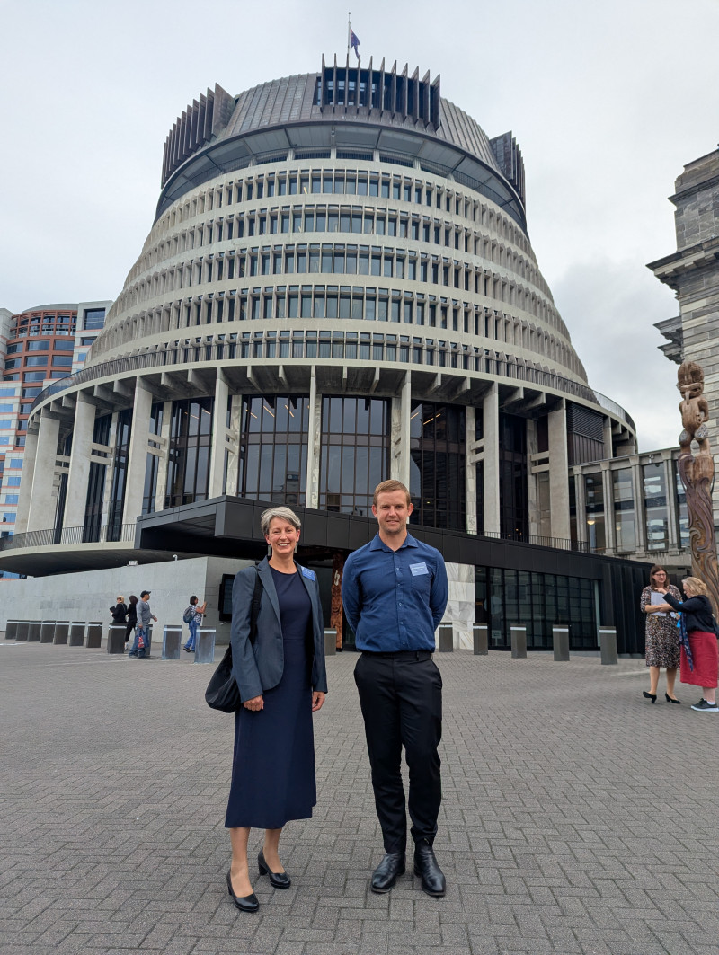 a formally-dress woman and man stand with the beehive towering over them
